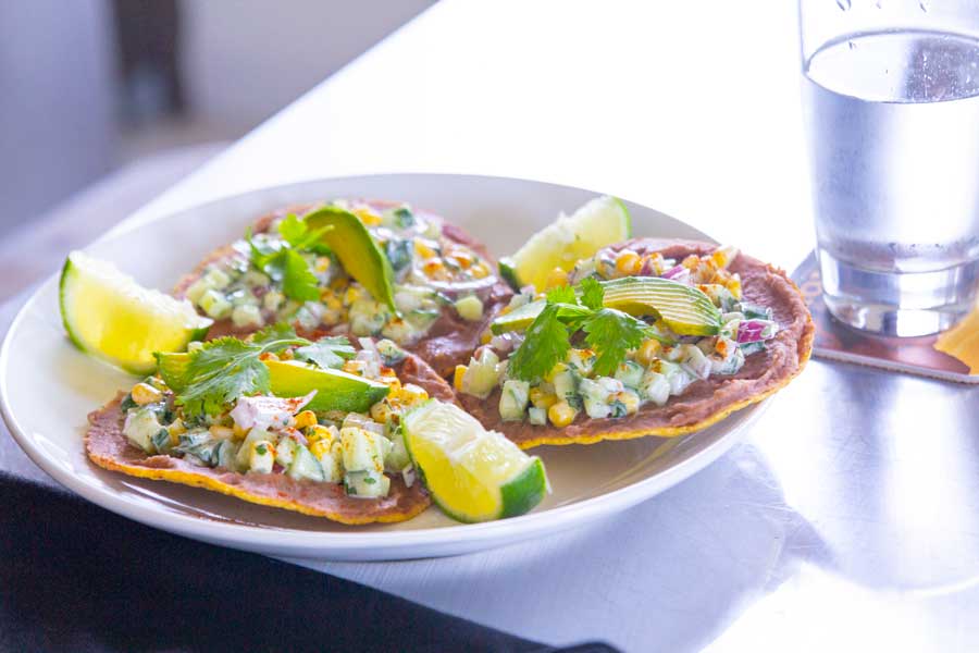 The corn and pinto bean tostadas garnished with slices of avocado, cilantro, and lime wedges.