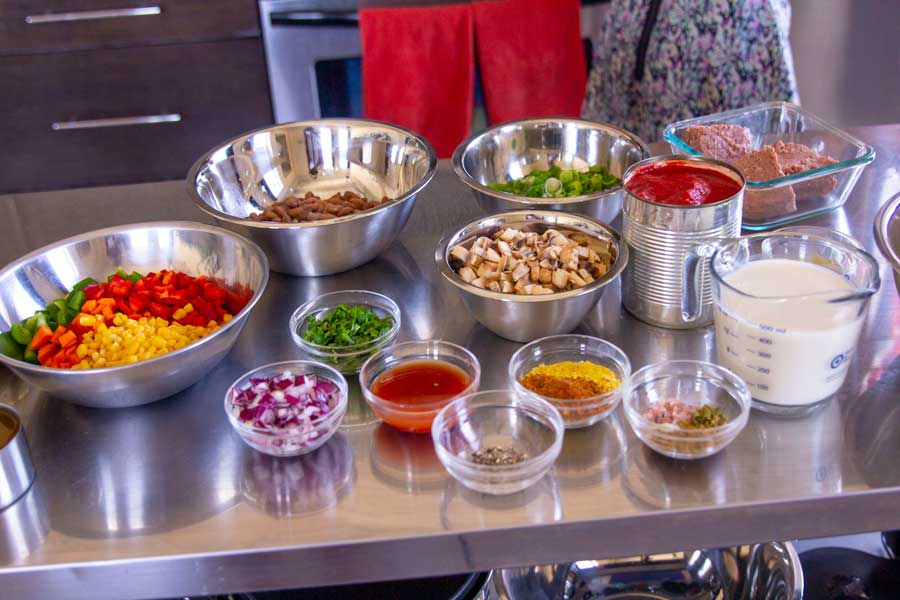 Spicy vegan chili ingredients laid out on the table such as: tomato sauces, chopped peppers, corn, onion, mushrooms, seasonings, tomato sauce and veggie grounds.