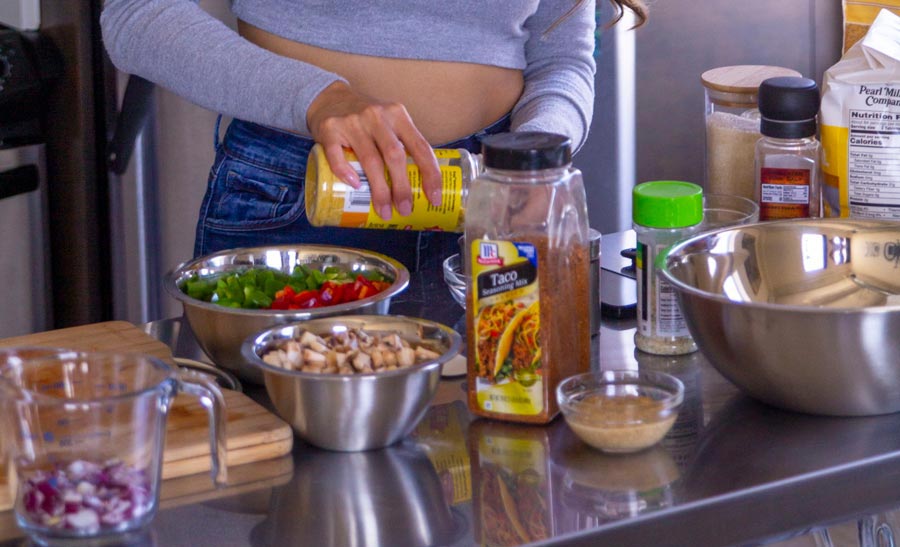 A spread of chopped veggies such as: mushrooms, bell peppers and red onion. Other seasonings are displayed such as taco seasoning for Spicy Vegan Chili.