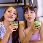 The Sol Sisters drinking a spirulina green smoothie in their kitchen.